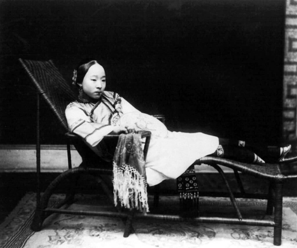 China: A young woman with bound feet reclining on a chaise longue, 1890