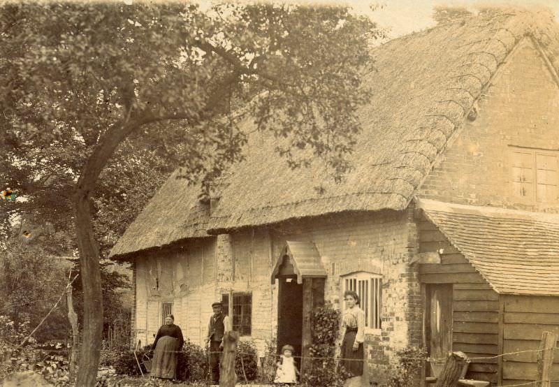 Family stand outside thatched house
