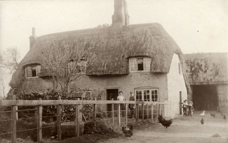 The farmers stand outside the front door and their children at the side with the hens and ducks pecking about