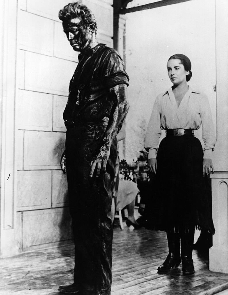 Elizabeth Taylor gazes at a begrimed James Dean (1931-1955) in a scene from the film 'Giant