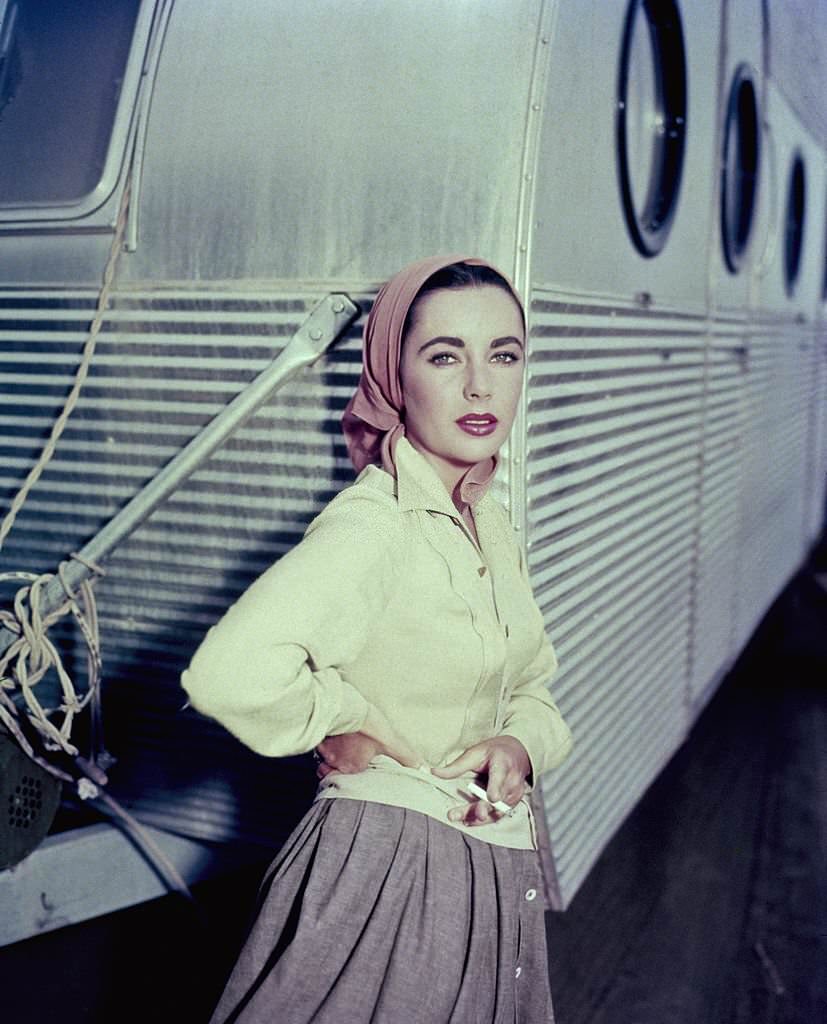 Elizabeth Taylor leaning against a dressing room trailer while smoking a cigarette on the set of 1956 film, 'Giant'.