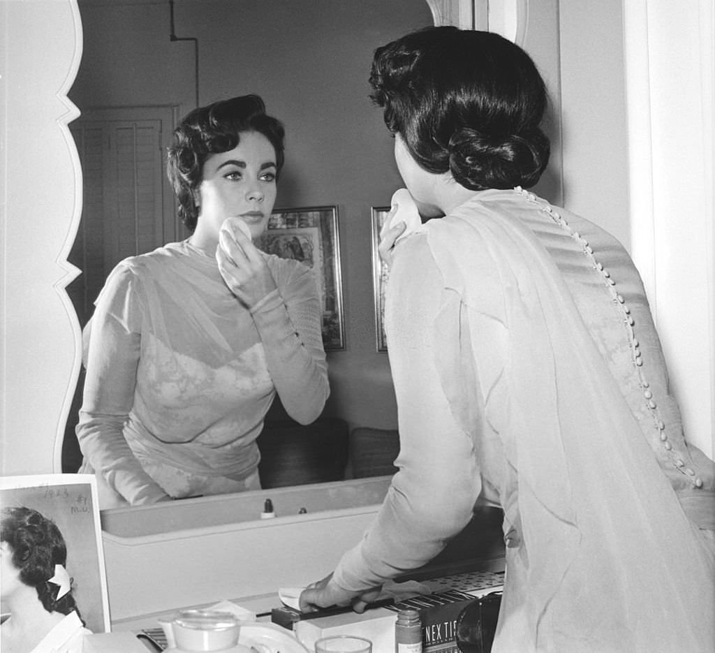 Elizabeth Taylor applies make-up in front of a mirror while on the set 'Giant'