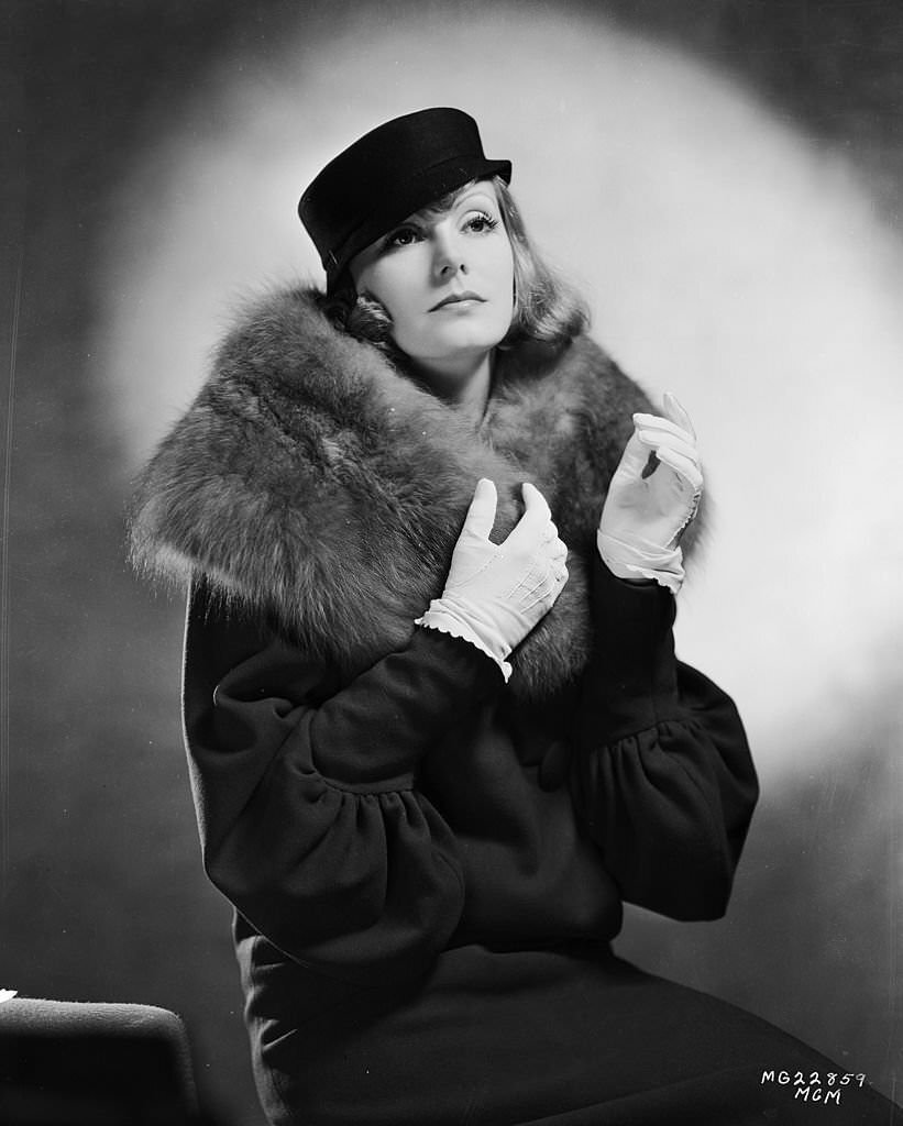 Greta Garbo wearing a coat with a fur collar and a small hat with a flat crown for her role as Grusinskaya in 'Grand Hotel', 1932