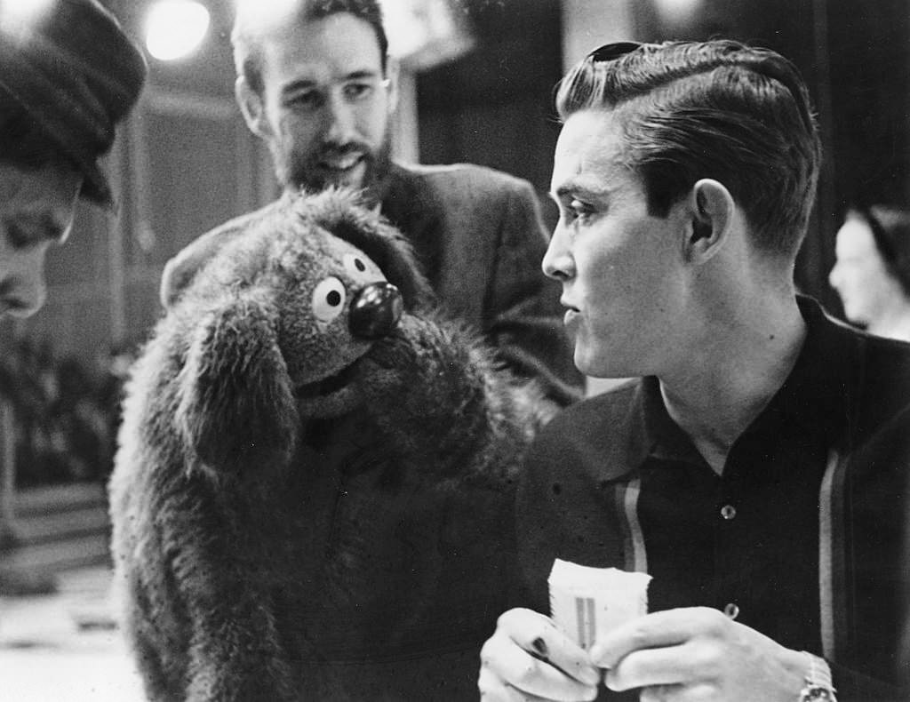 Muppets creator Jim Henson, (beard, background), manipulates one of his creations as it engages in conversation with singer Jimmy Dean in 1963.