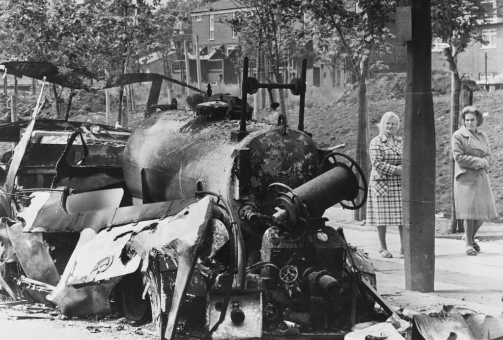 Two women walk past the burnt wreck of a fire engine following a night of rioting in the Toxeth area of Liverpool, England, 7th July 1981.