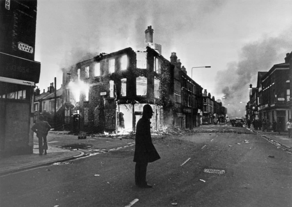 A police officer is silhouetted against a background of a burning building during riots in the Toxteth area of Liverpool, England, 8th July 1981.