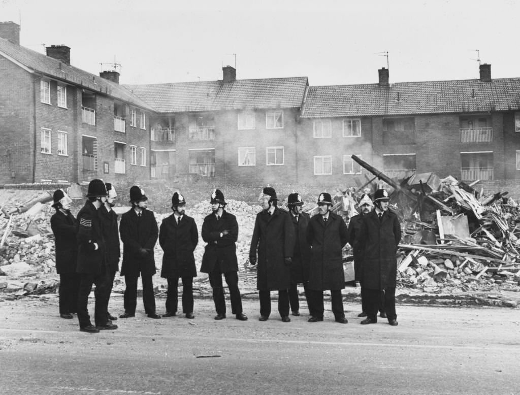 A group of police officers stand before the rubble of a wrecked building after a night of rioting in the Toxteth area of Liverpool, July 1981.