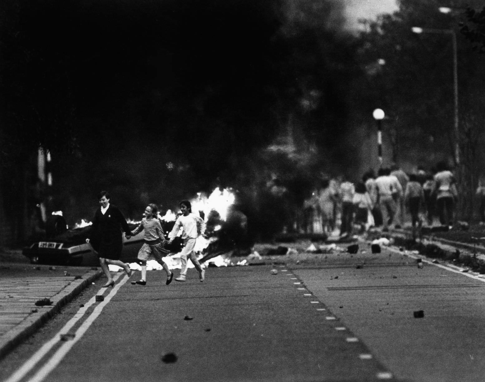 Toxteth Riot 1st October 1985 Children crossing the street as the riot goes on in the background on Princes Road, Toxteth