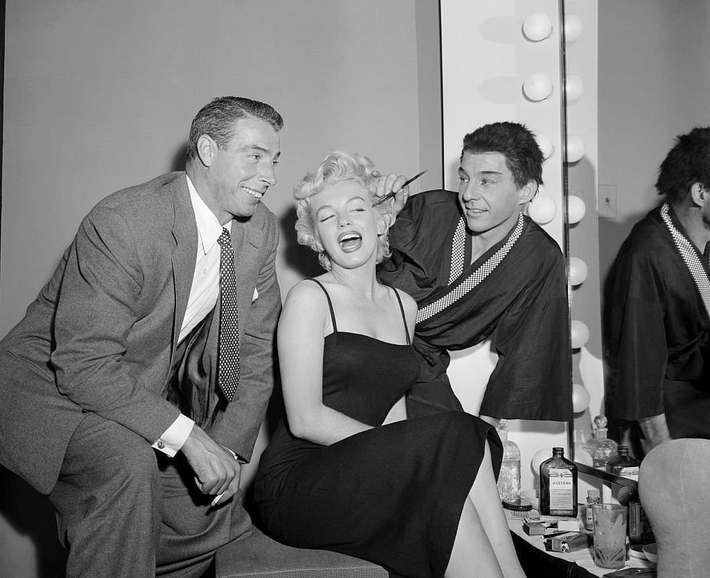 David Wayne applies makeup to Marilyn Monroe while her husband Joe DiMaggio looks on.