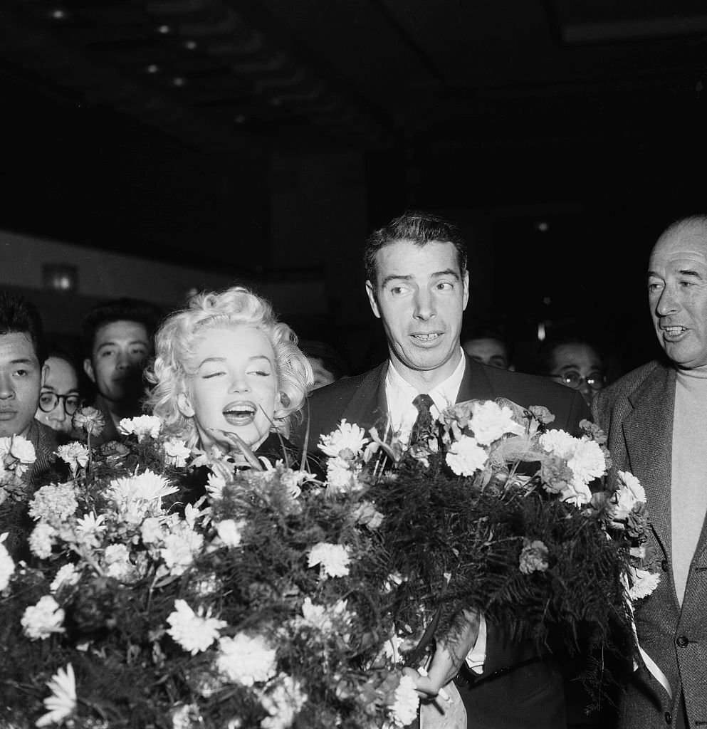 Marilyn Monroe and Joe DiMaggio receive flower bouquets upon their arrival in Tokyo, where the famous couple will be spending their honeymoon.