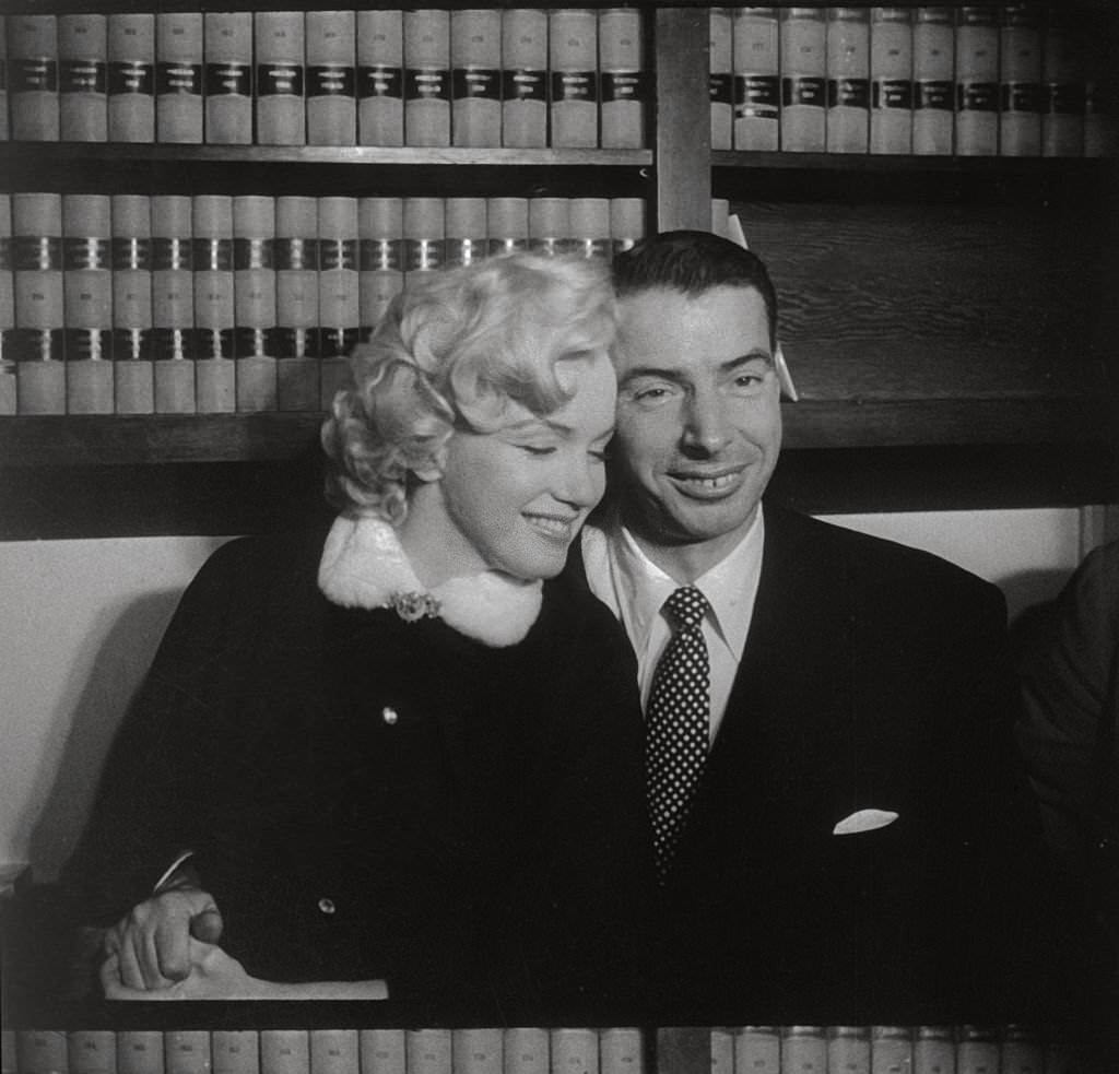 Marilyn Monroe and Joe DiMaggio sitting close together.