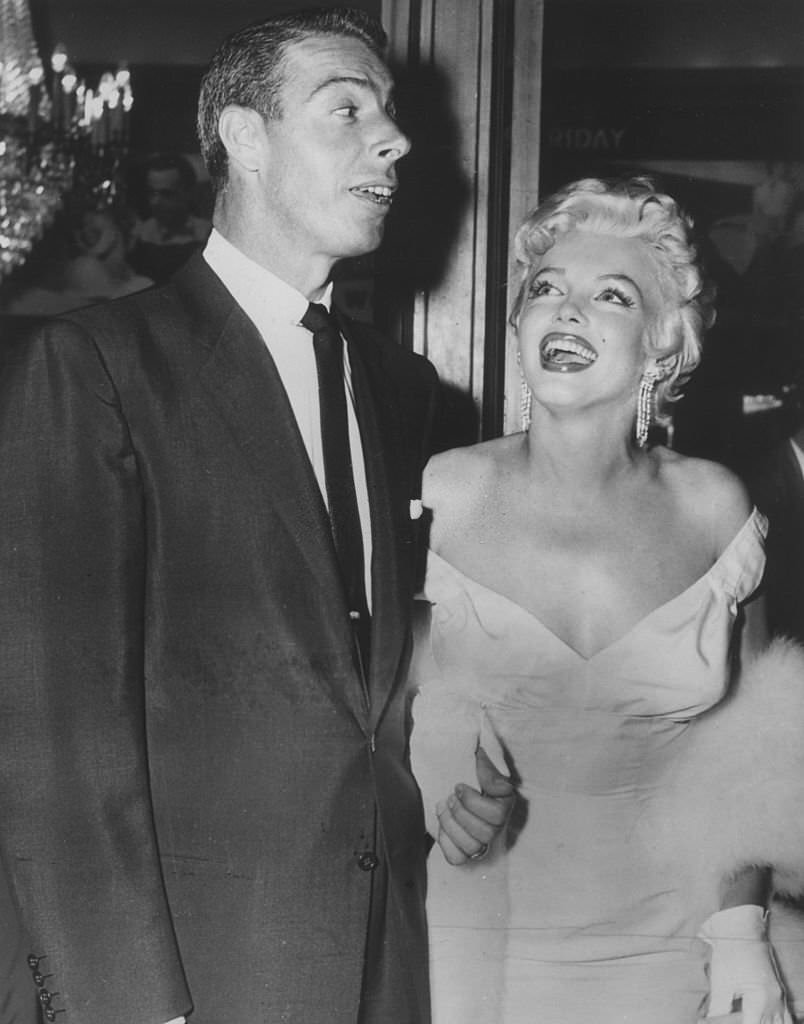Marilyn Monroe wearing a low-cut white evening gown, with Joe DiMaggio.