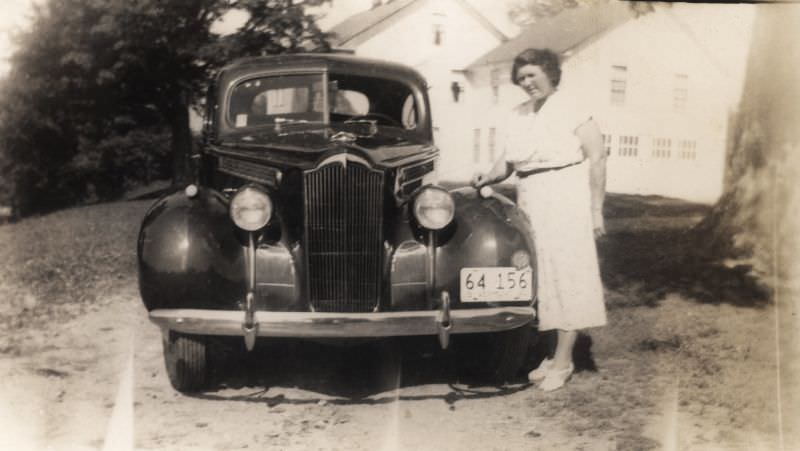 An elderly lady in a white short-sleeved dress posing with a 1940 Packard.