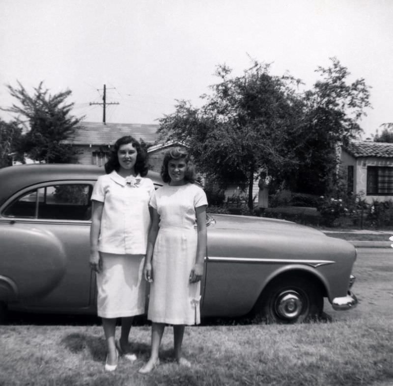 Two young women in white – probably dressed for a special occasion – posing with a 1951-52 Packard 200 Sedan.