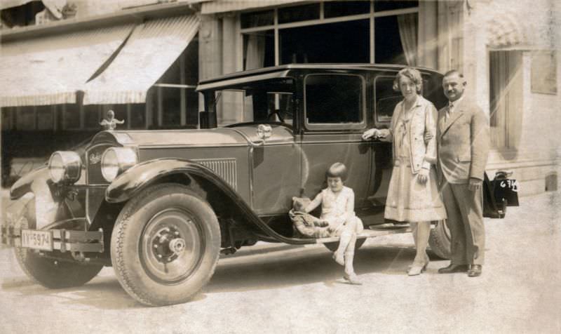 A well-to-do family of three posing with a 1928 Packard Standard Eight Sedan in summertime.