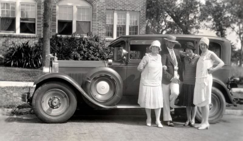 Four stylish individuals posing with a 1928 Packard Sedan in front of a large brick-built house in summertime, 1928