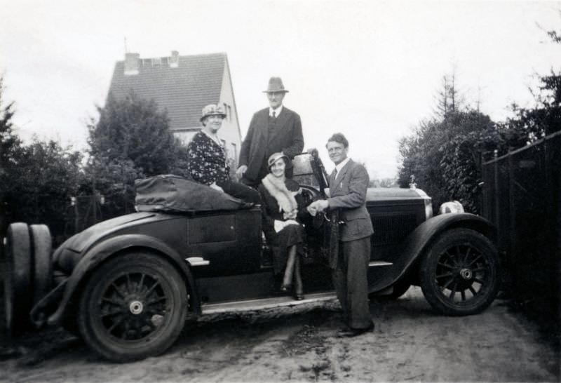 Two elegant couples posing with a 1926 Packard Roadster open-topped in a residential street on the outskirts of town, 1928
