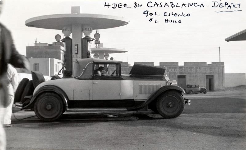 A 1930 two-tone Packard Standard Eight Convertible Coupe convertible refueling at a Shell filling station in early morning sunlight, December 4, 1934