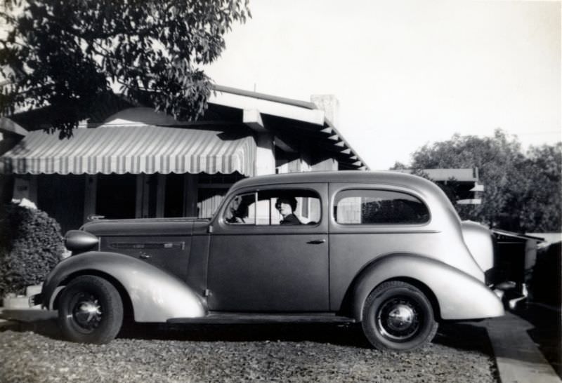 A stylish lady posing in the driver's seat of a 1936 Pontiac Deluxe Six in the drive of a private home.