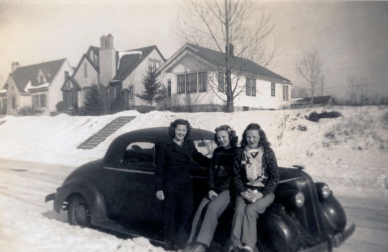 Three ladies, probably a mother and her daughters, posing with a 1936 Pontiac Business Coupe on a snow-covered road on a sunny winter's day, 1936