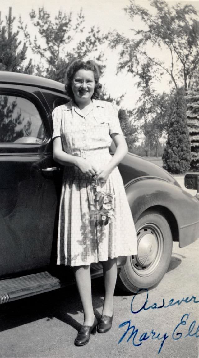 A young lady with a bunch of flowers in her hands posing with a 1938 Pontiac.