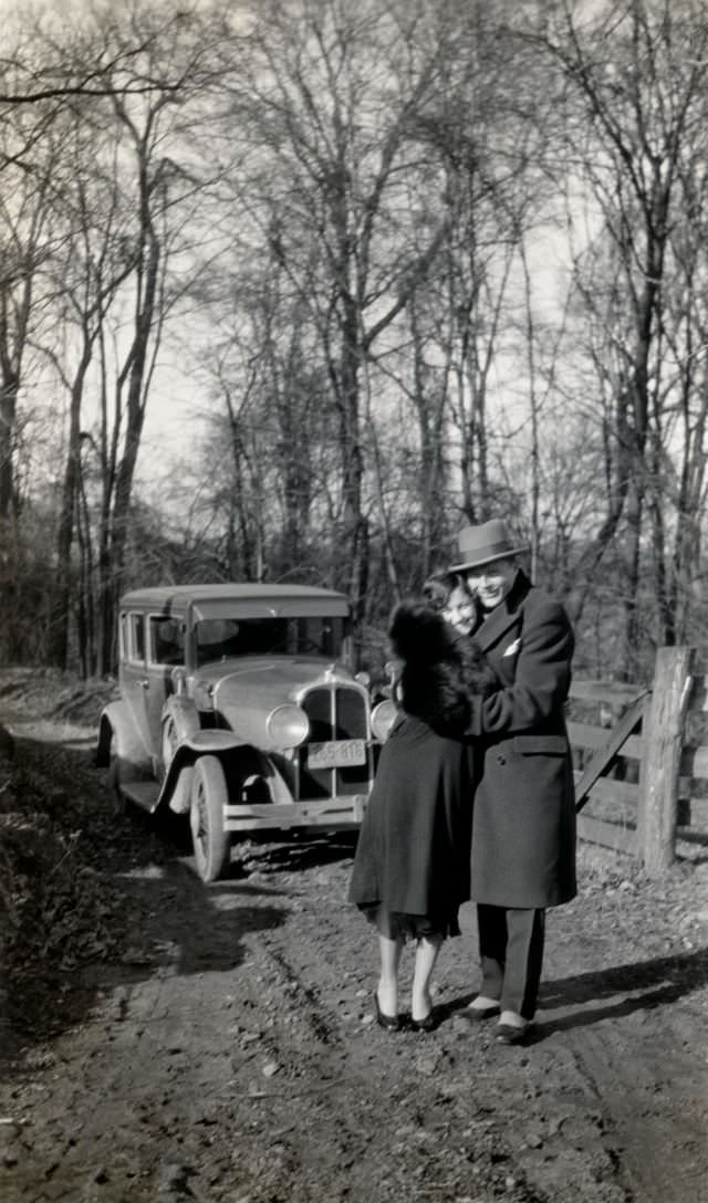 A stylish couple embracing in front of a 1929 Pontiac on a rural driveway in wintertime, 1929