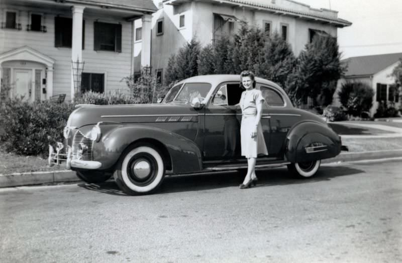 A young lady posing with a 1940 Pontiac Torpedo Eight Sport Coupe in a residential street, 1940