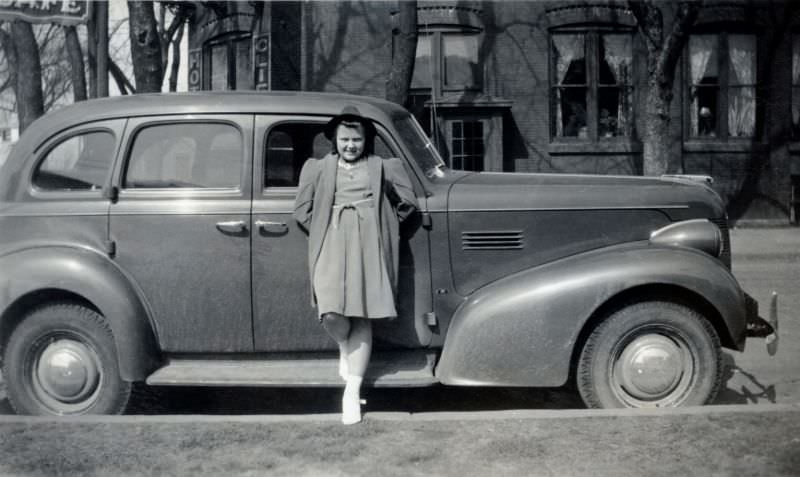 An adolescent girl dressed in the fashion of the late thirties seductively posing with a Pontiac in wintertime, 1940