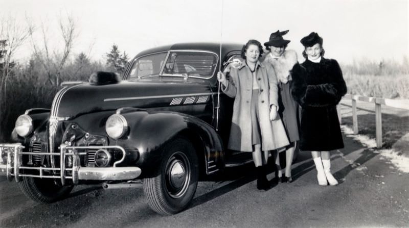 Three stylish ladies posing with a 1940 Pontiac on a sunny winter's day, 1940