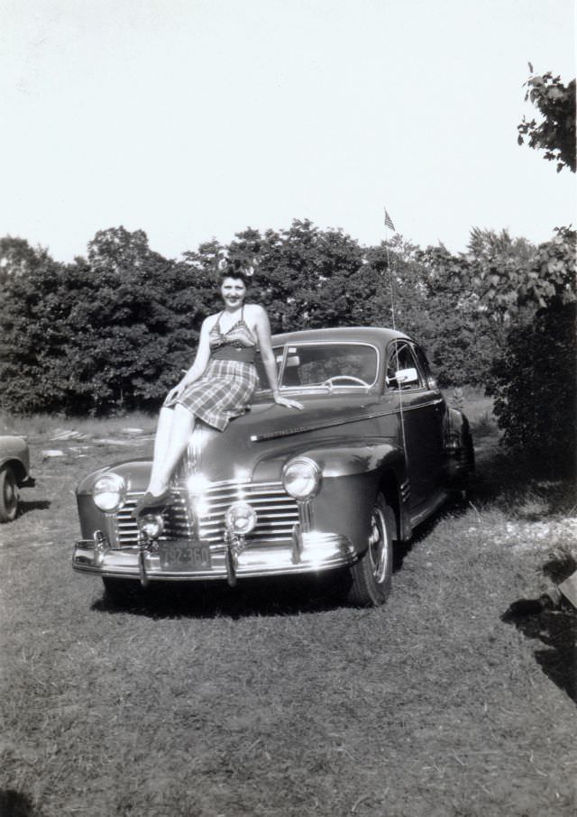 A young lady in a checkered dress with flowers in her hair posing on the bonnet of a 1941 Pontiac Custom Torpedo Six Coupe.