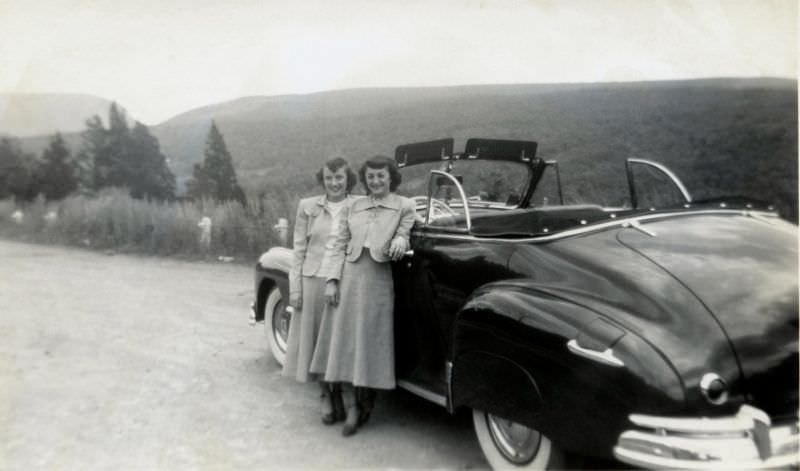 Two ladies, probably mother and daughter, posing with a 1948 Pontiac Torpedo Deluxe Convertible on a gravel road in the countryside.