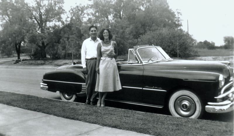 A fellow in a white shirt and a lady in a summer dress posing with a 1949 Pontiac Chieftain Eight Convertible.