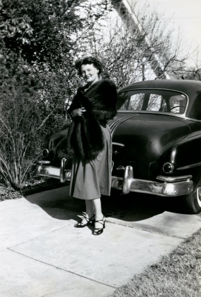 An elegant lady posing with a 1949 Pontiac Sedan in the drive of a suburban home.