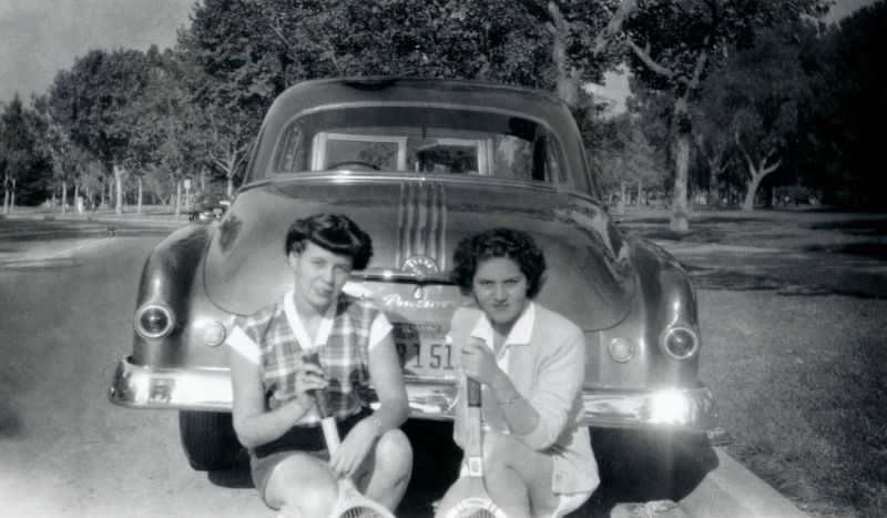 Two fashionable ladies posing with a 1950 Pontiac Chieftain Sedan in summertime.