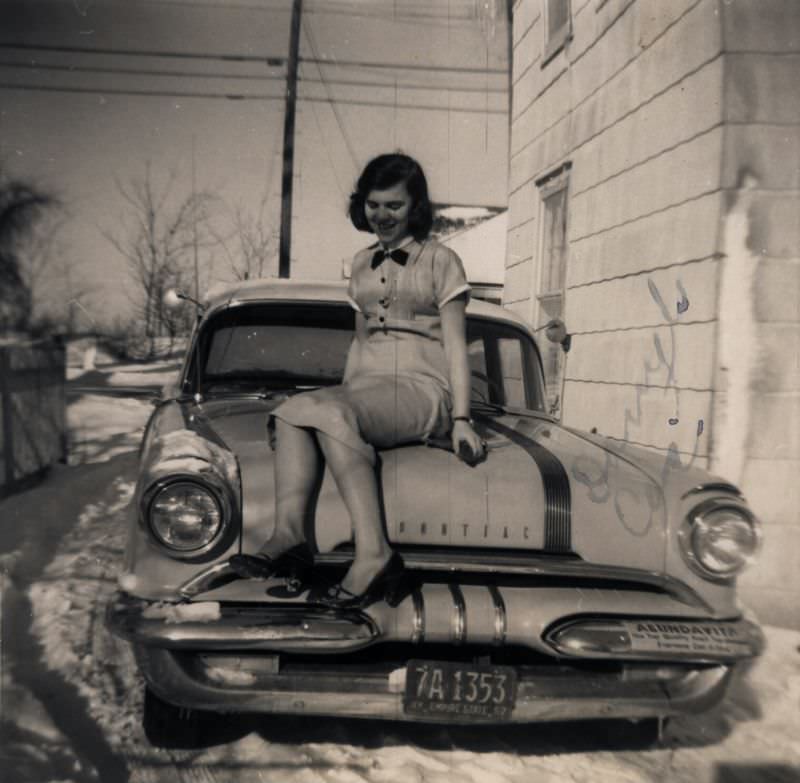 A girl posing on the hood of a 1955 Pontiac Chieftain in wintertime.