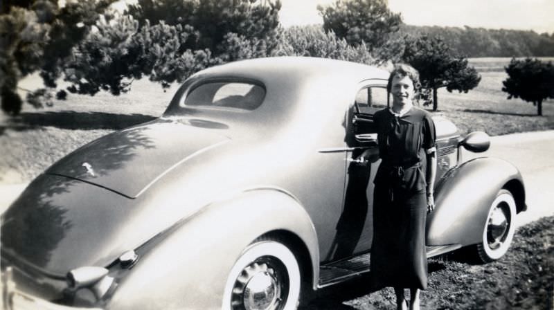 A cheerful lady posing with a 1936 Pontiac Coupe in the countryside, 1936
