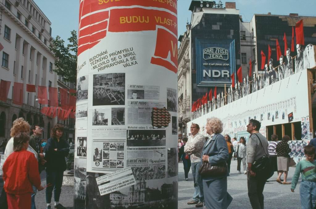 People walking past a column showcasing political handouts, Prague, Czech Republic, June 1990.