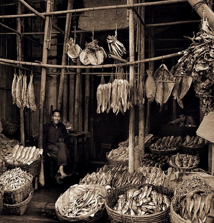 Seated Man Amid Baskets of Fish & Hanging Dried Fish, Eastern Districts, Hong Kong Island, 1946