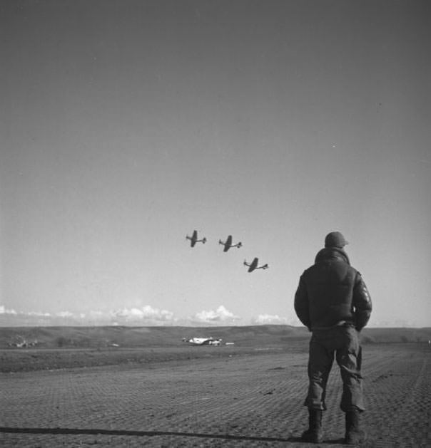 A Tuskegee airman standing on an airfield, looking at airplanes