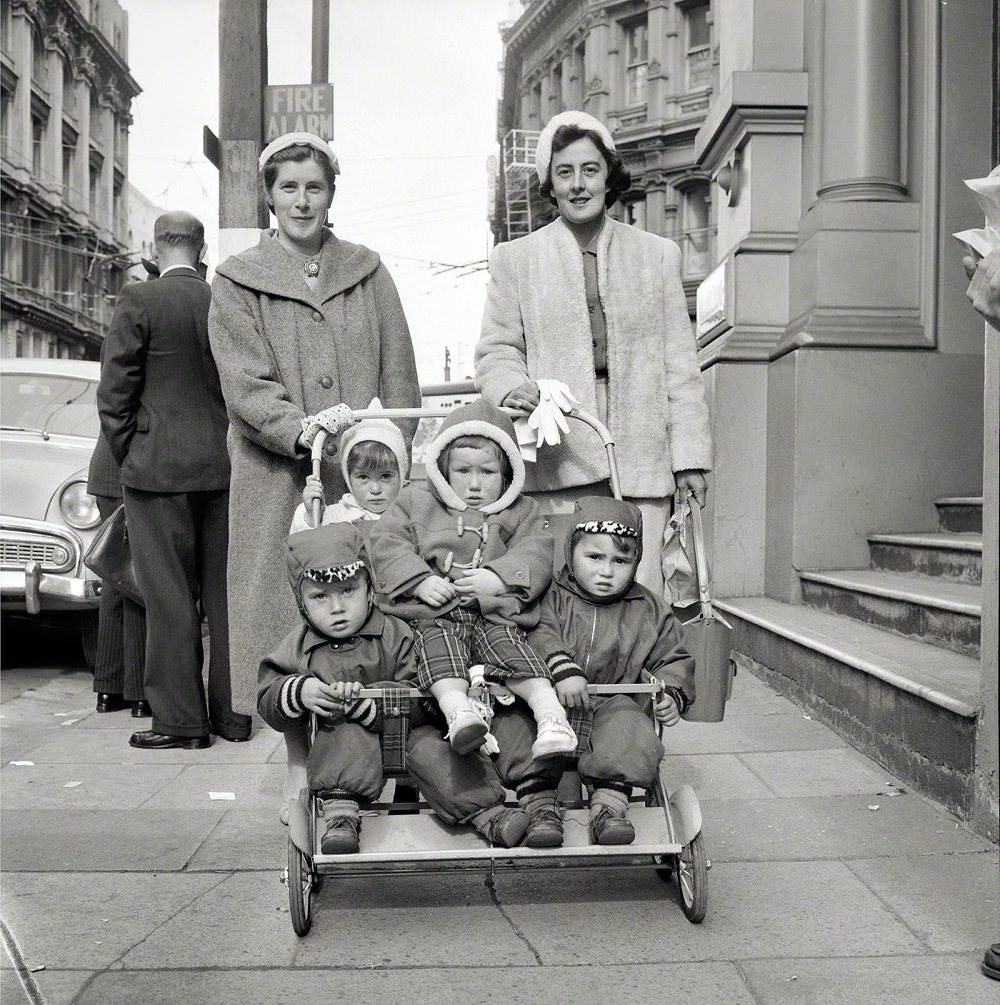Two women with four small children in a pushchair on a city street, Wellington, New Zealand, Aug. 21, 1959