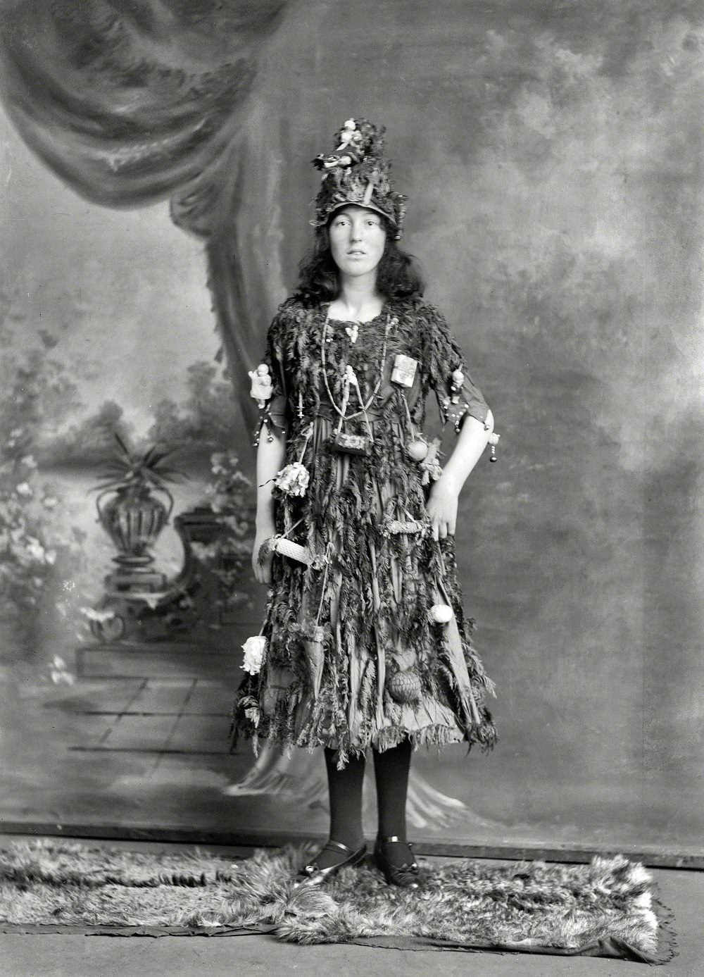 Young woman in Christmas tree fancy dress and hat costume, with little presents and decorations hanging off her, Christchurch, New Zealand circa 1910