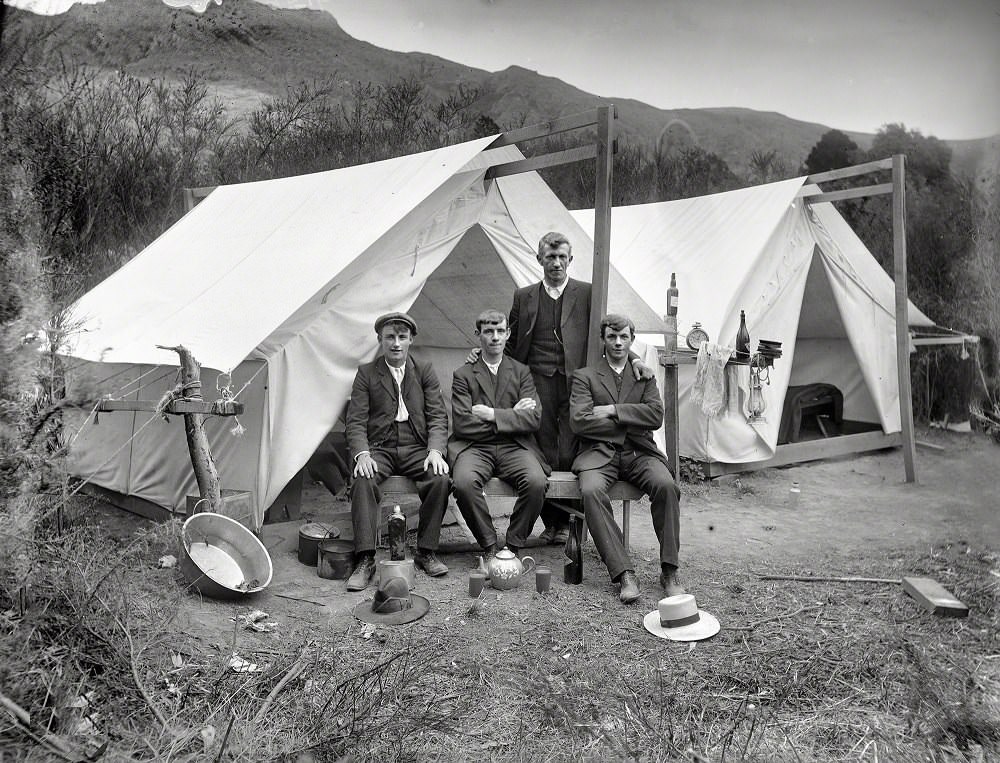 Four unidentified men in front of a tent, showing a washing basin, pots and teapot with cups of tea, camping ground unidentified, possibly Christchurch district, 1915