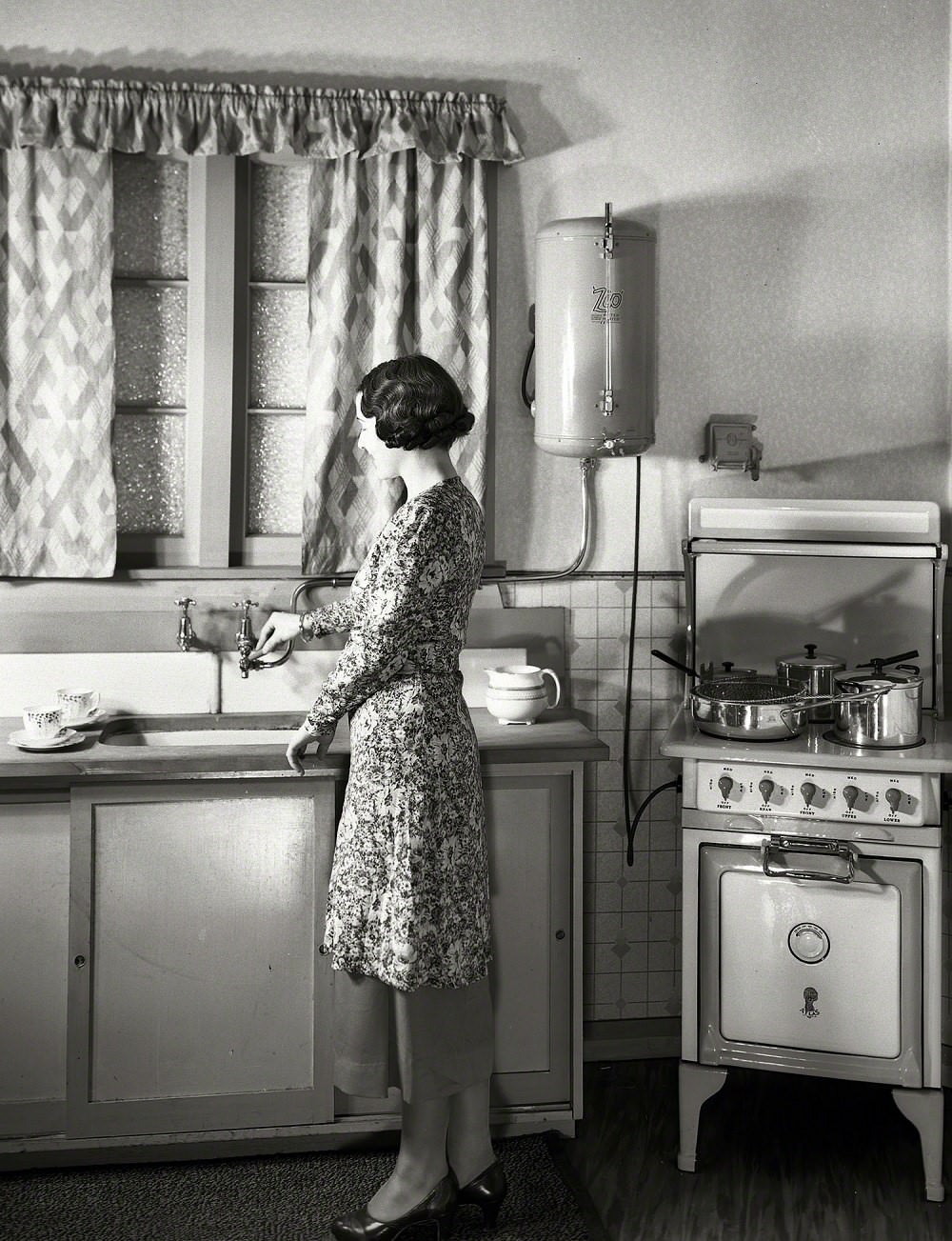 Model at sink in kitchen equipped with Atlas electric stove and Zip water heater, Wellington, New Zealand circa 1930s