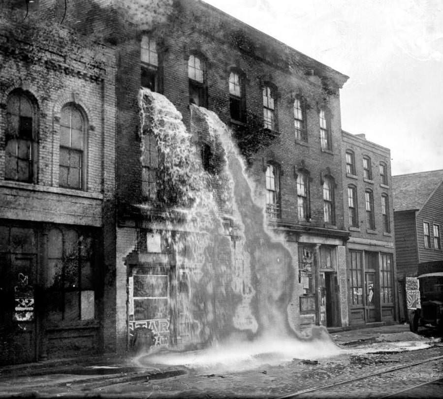 Alcohol, discovered by Prohibition agents during a raid on an illegal distillery, pours out of the windows of a storefront in Detroit, 1929.