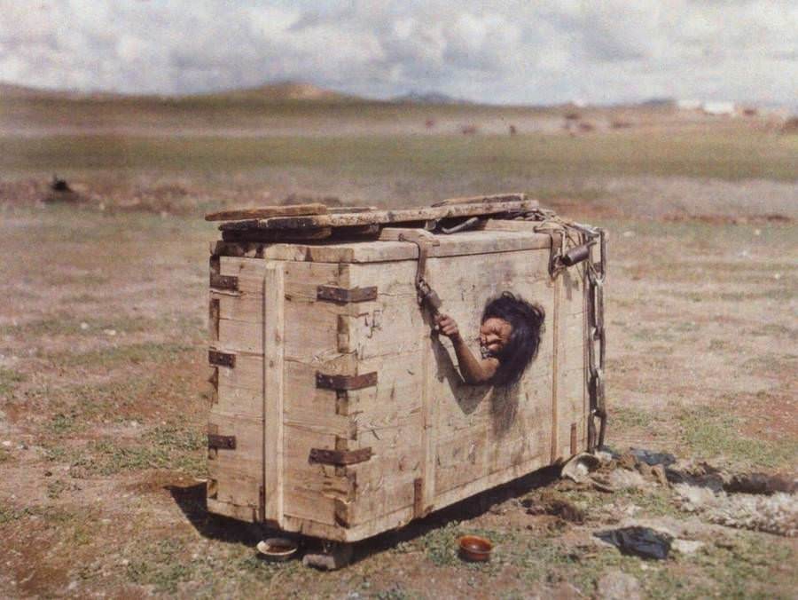 A Mongolian woman sits trapped inside a wooden box as a form of punishment, 1913.