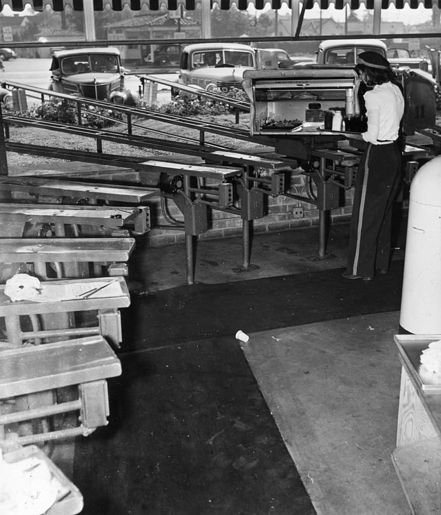 A woman loads a box, which will deliver food to a waiting car at a drive-in restaurant in Hollywood, 1955