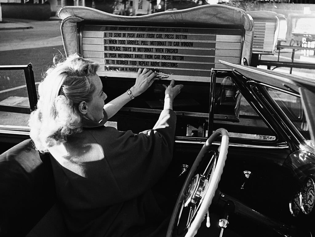 A woman sitting in her convertible removes a lunch tray from the Auto-Motor mart.
