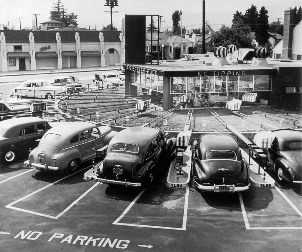 Cars parked at an automated drive-in diner, where individual conveyor belts transport food directly to the driver, Califonia, 1950.