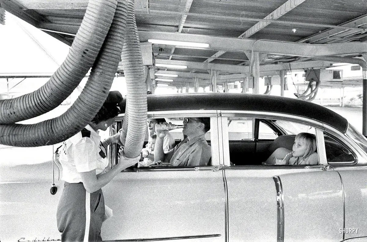 A family at a drive-in restaurant has cool air piped into their car. 1957.