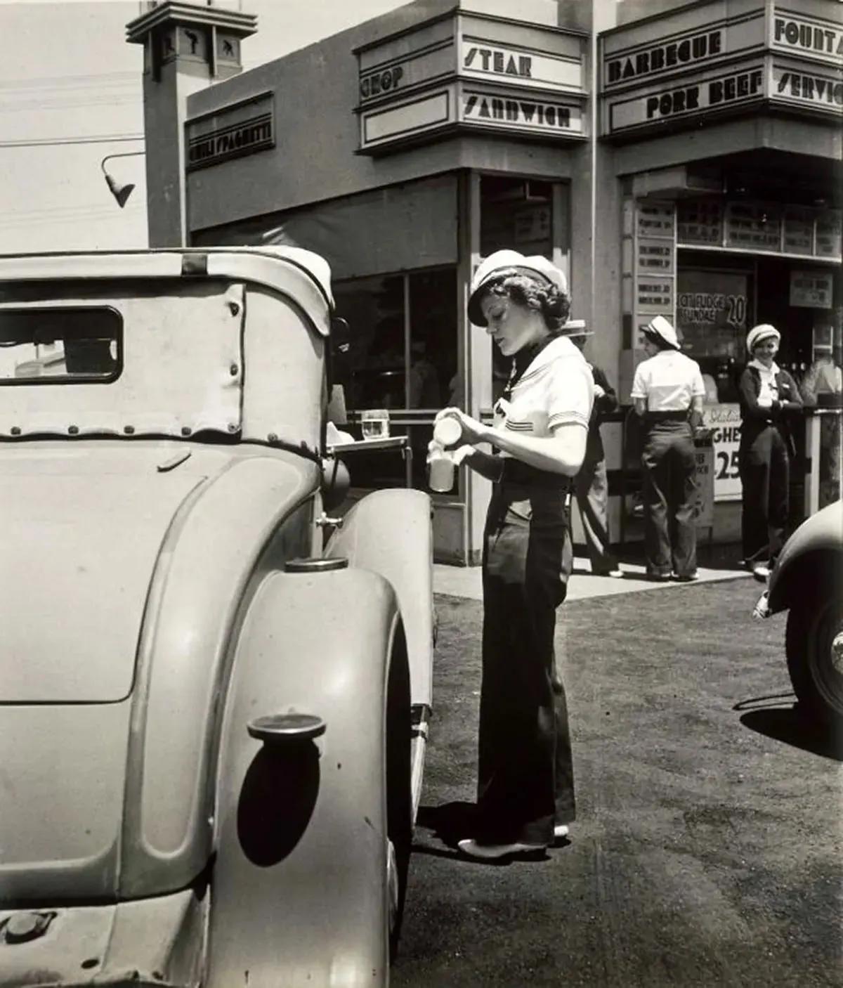 A carhop pouring milk from a bottle into a glass, at McDonnell’s Drive-In. 1930s.